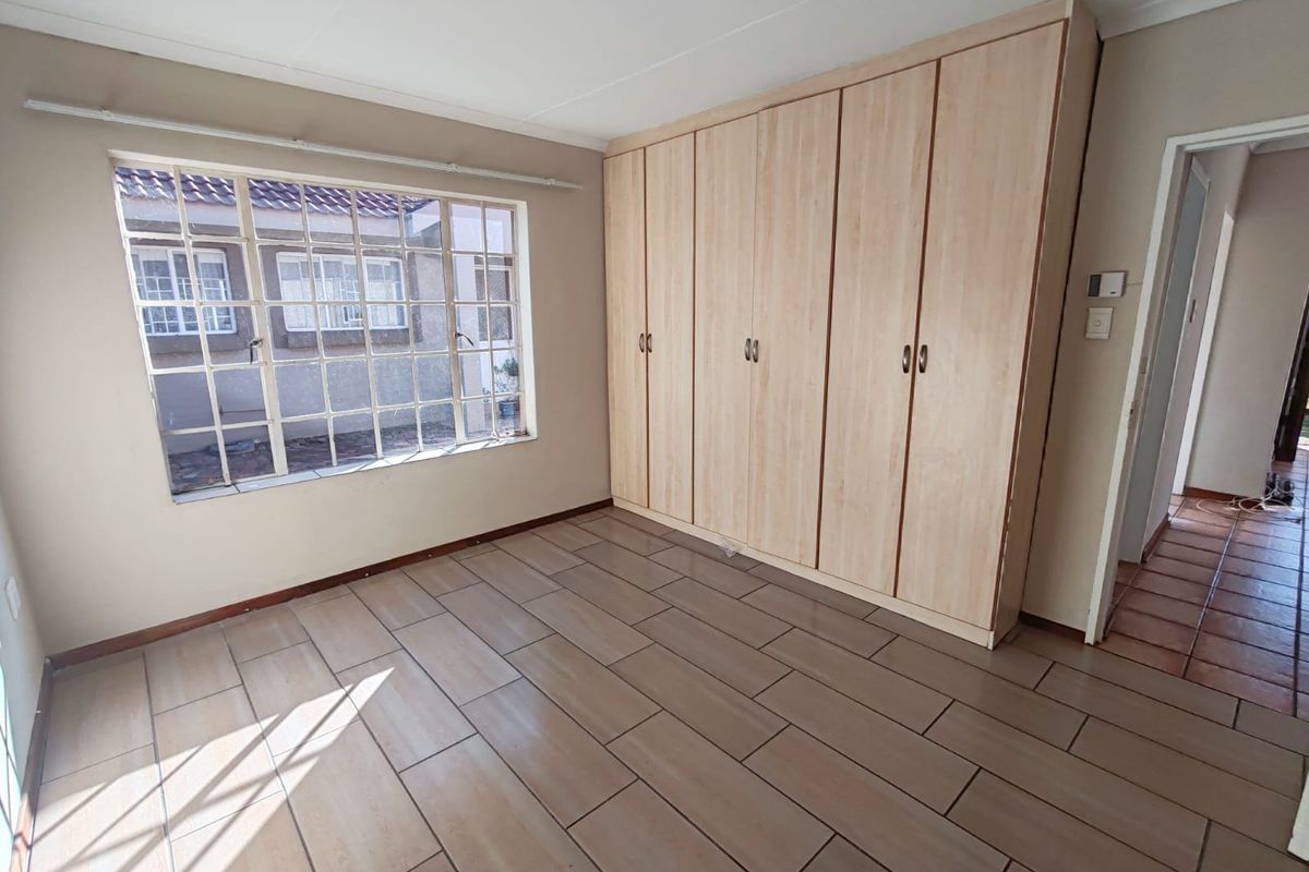 A bright bedroom featuring light wood-look floor tiles and extensive built-in cabinetry, offering ample storage space and natural light.