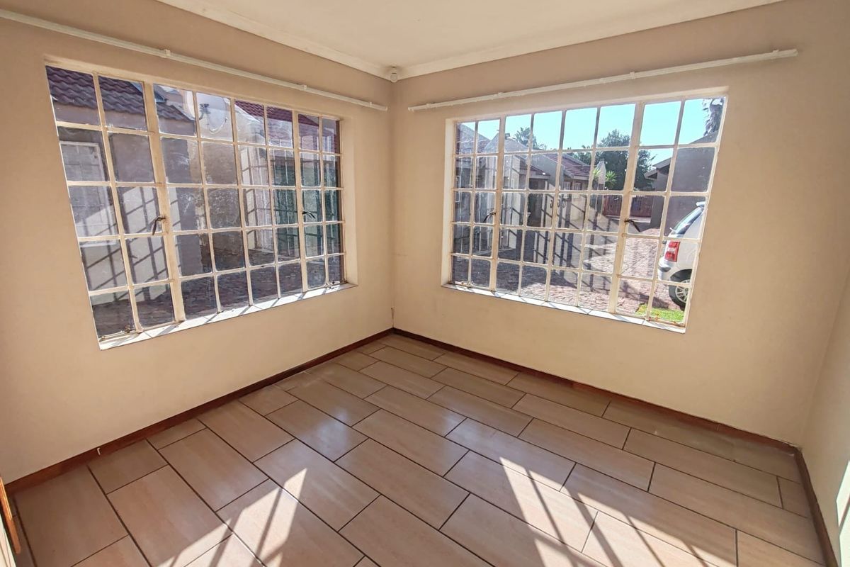 A bright, empty living room featuring large steel-framed windows and neutral ceramic floor tiling, offering a versatile space for living or dining.