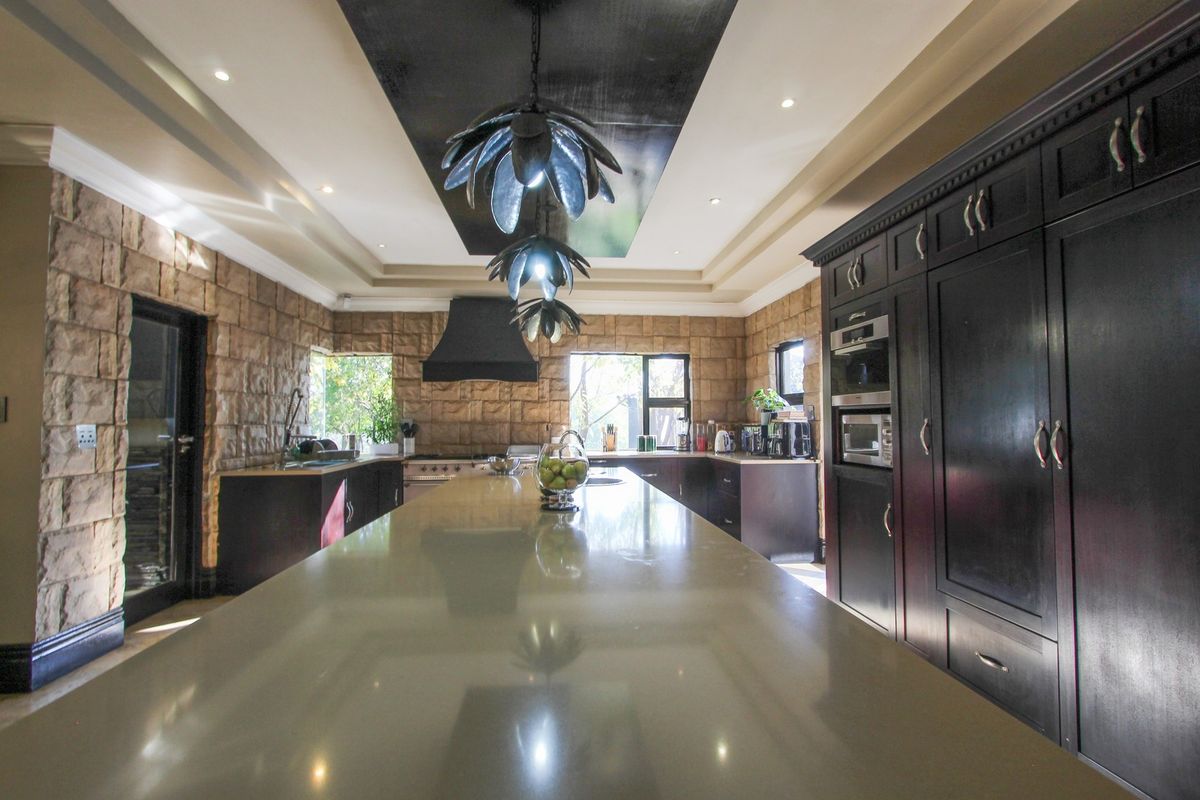 Spacious kitchen featuring a large central island, dark cabinetry, built-in oven and microwave, and distinctive stone-clad feature walls.