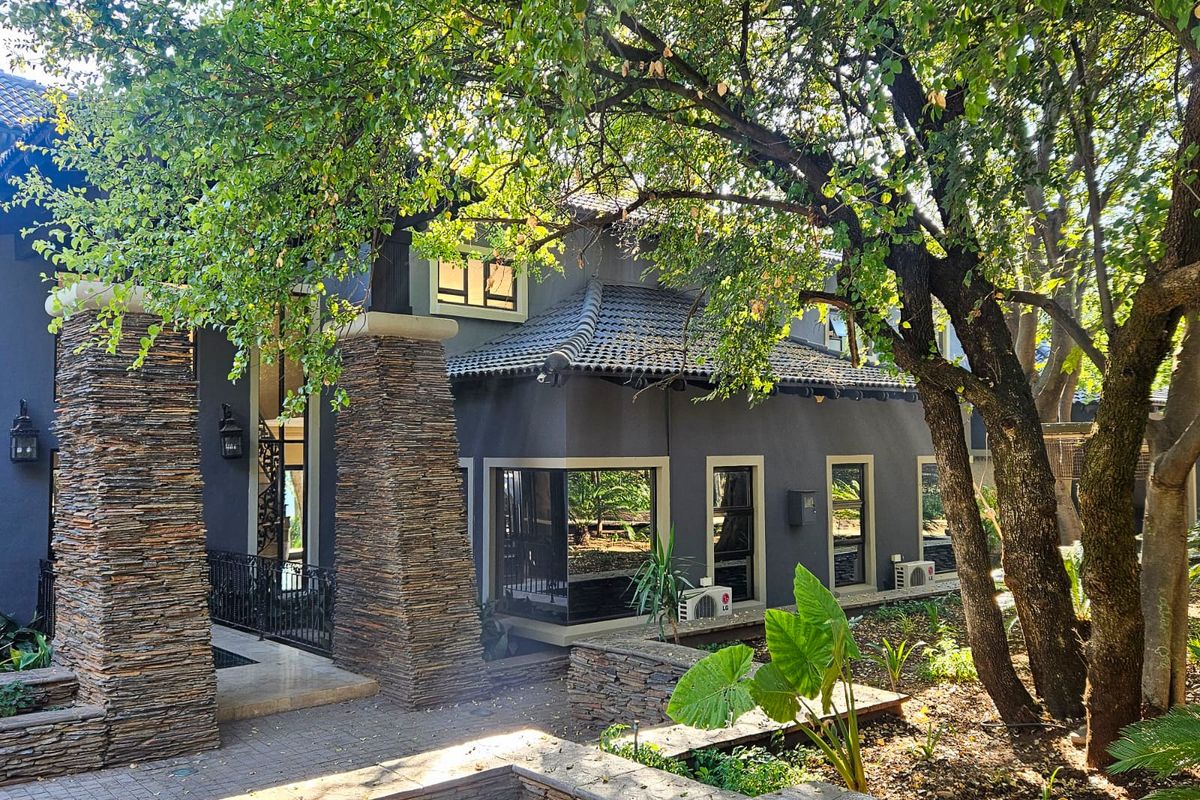 A view of the rear exterior facade featuring dark grey walls, stone-clad pillars, tiled roofing, and established garden landscaping.