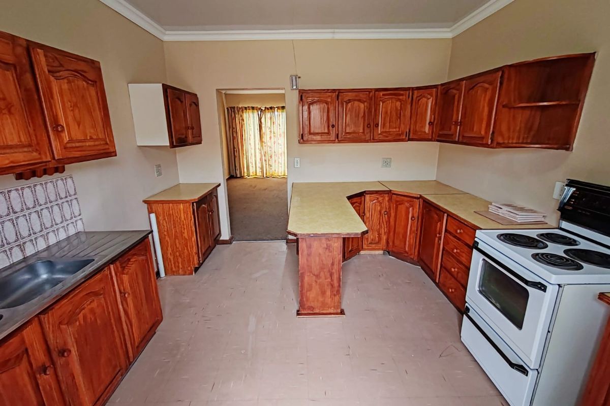 A functional kitchen featuring wooden cabinetry, laminate countertops, and a built-in stove, with a direct view into the adjacent living area.