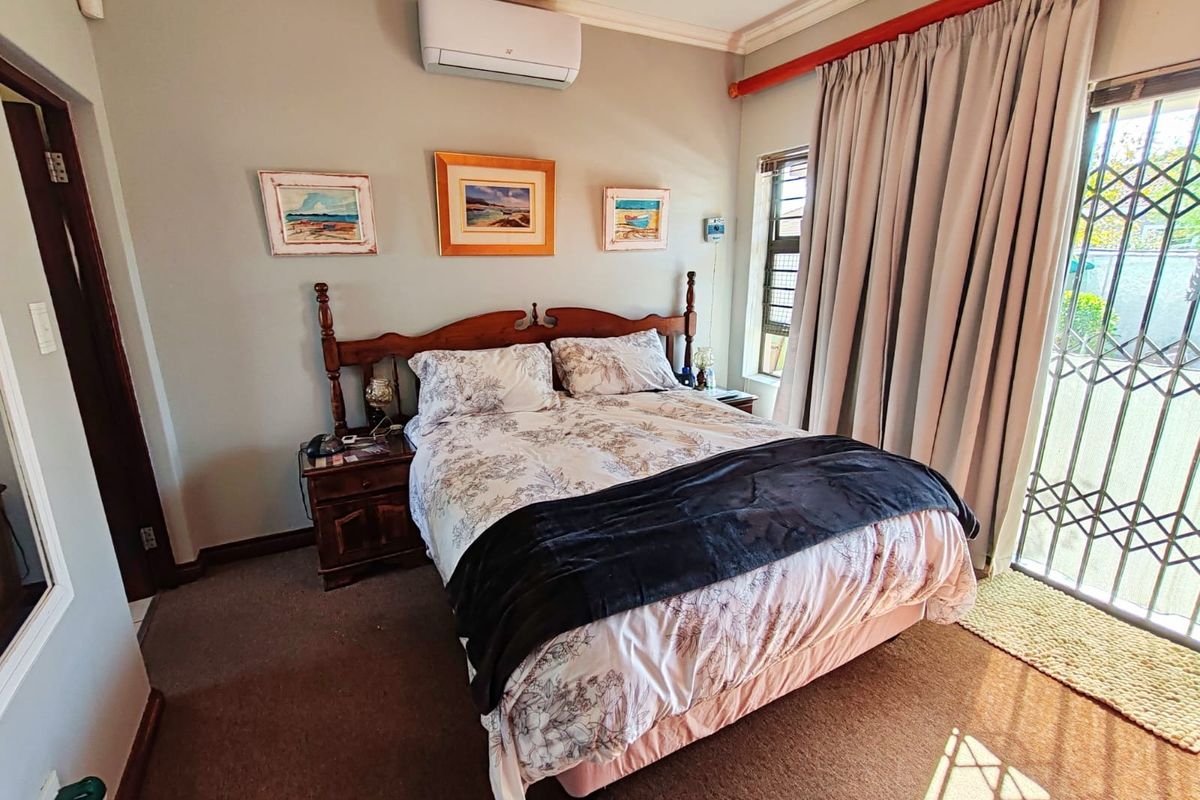 A bedroom featuring carpeted flooring, a wall-mounted air conditioning unit, and a sliding door with security gate providing access to the exterior.