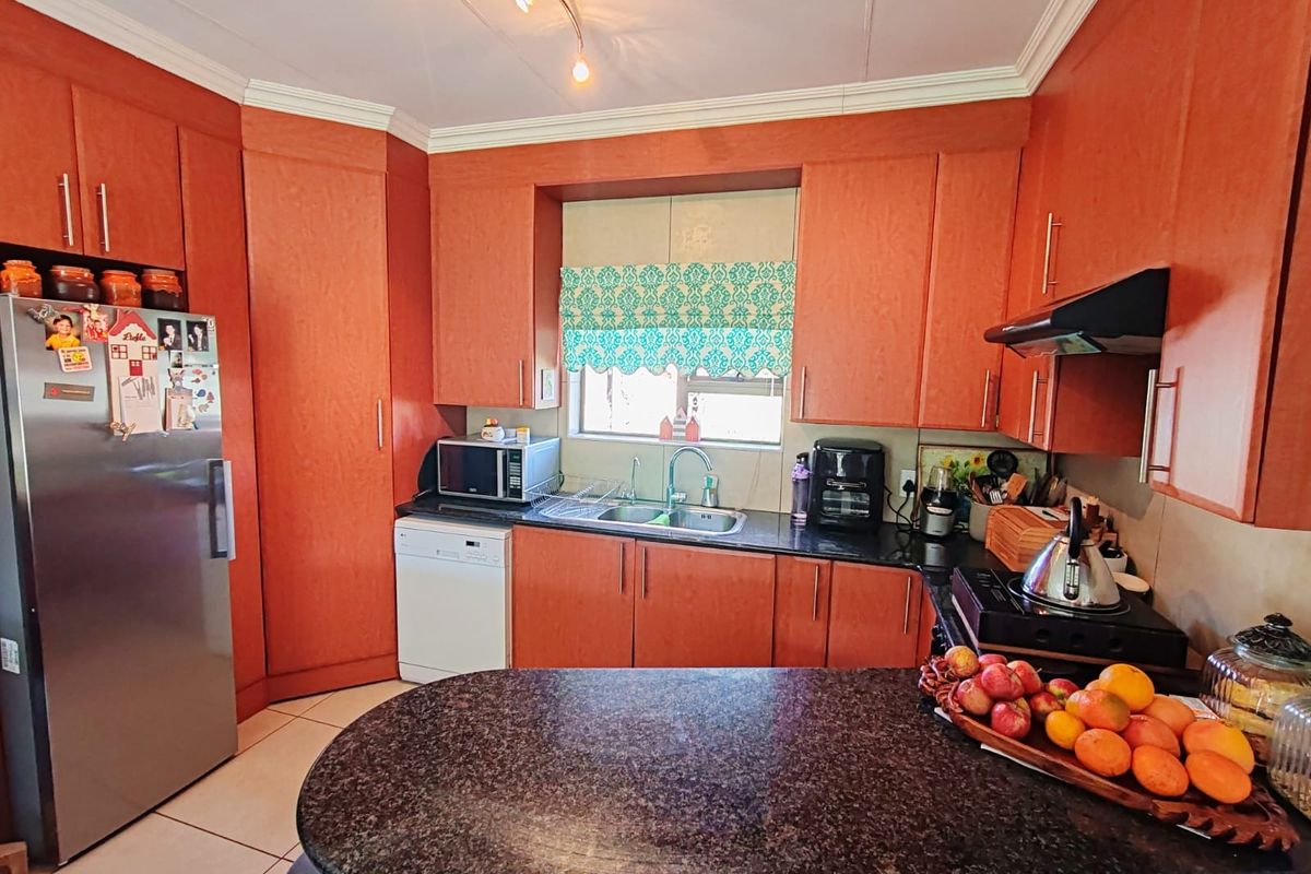 A functional kitchen featuring wood-finish cabinetry, granite countertops, a stainless steel sink, and an integrated extractor fan.