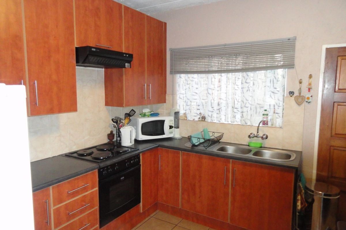 A functional kitchen featuring wood-look cabinetry, dark laminate countertops, a built-in oven, hob, extractor fan, and a double stainless steel sink.