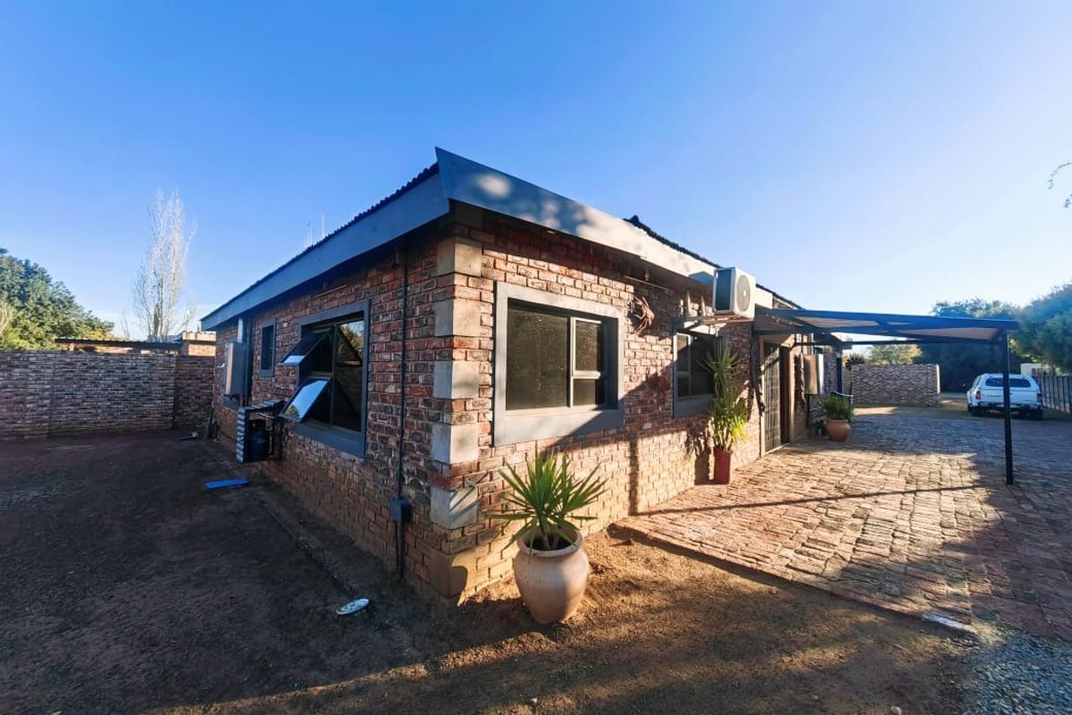 Exterior view of a face-brick house featuring a covered patio area, paved driveway, and wall-mounted air conditioning unit.