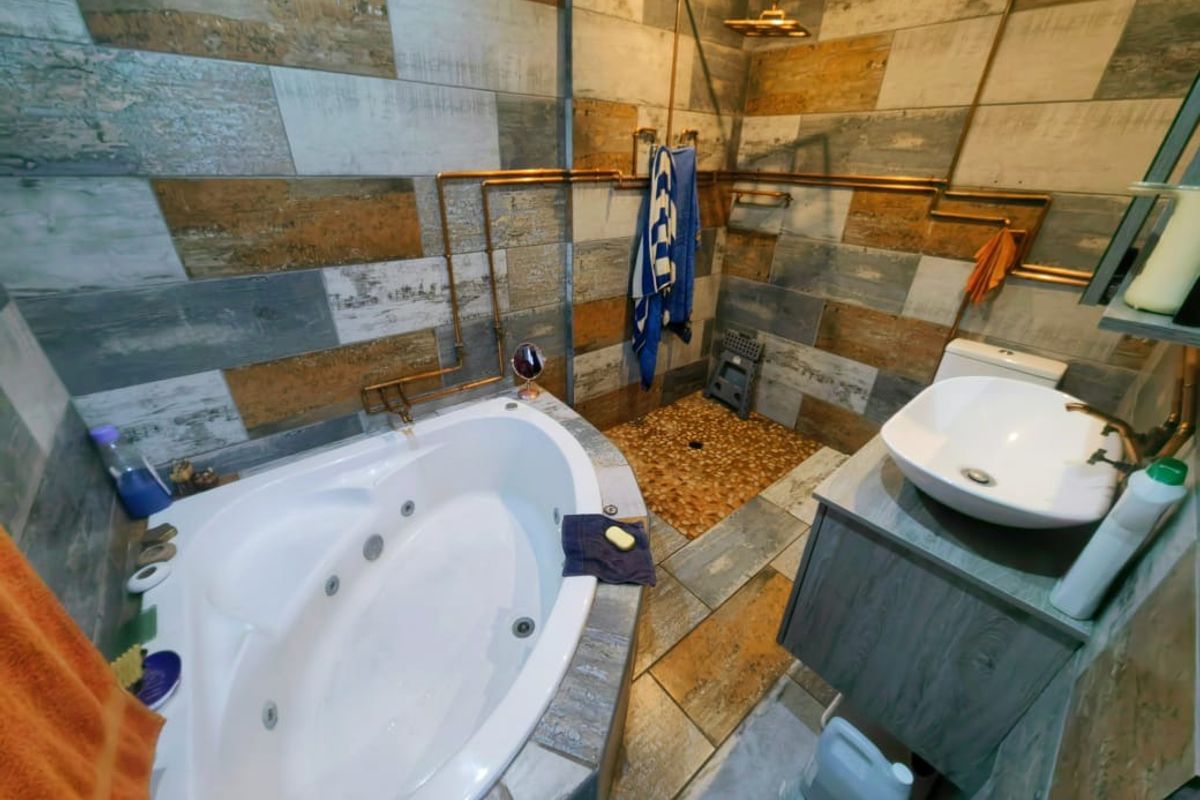 A bathroom featuring a corner jetted bathtub, a walk-in shower with pebble flooring, and a modern vessel sink vanity with rustic wood-look wall tiling.