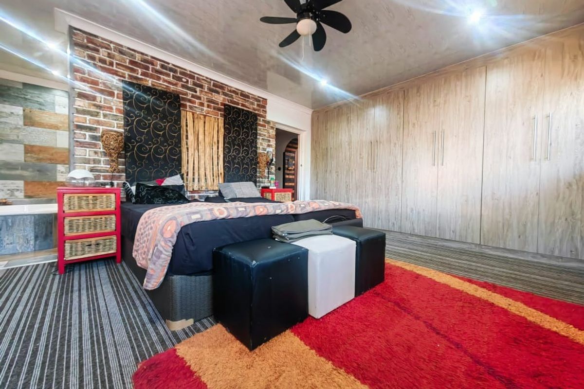 Spacious bedroom featuring a prominent exposed brick feature wall, extensive built-in timber-look cabinetry, and a ceiling fan.