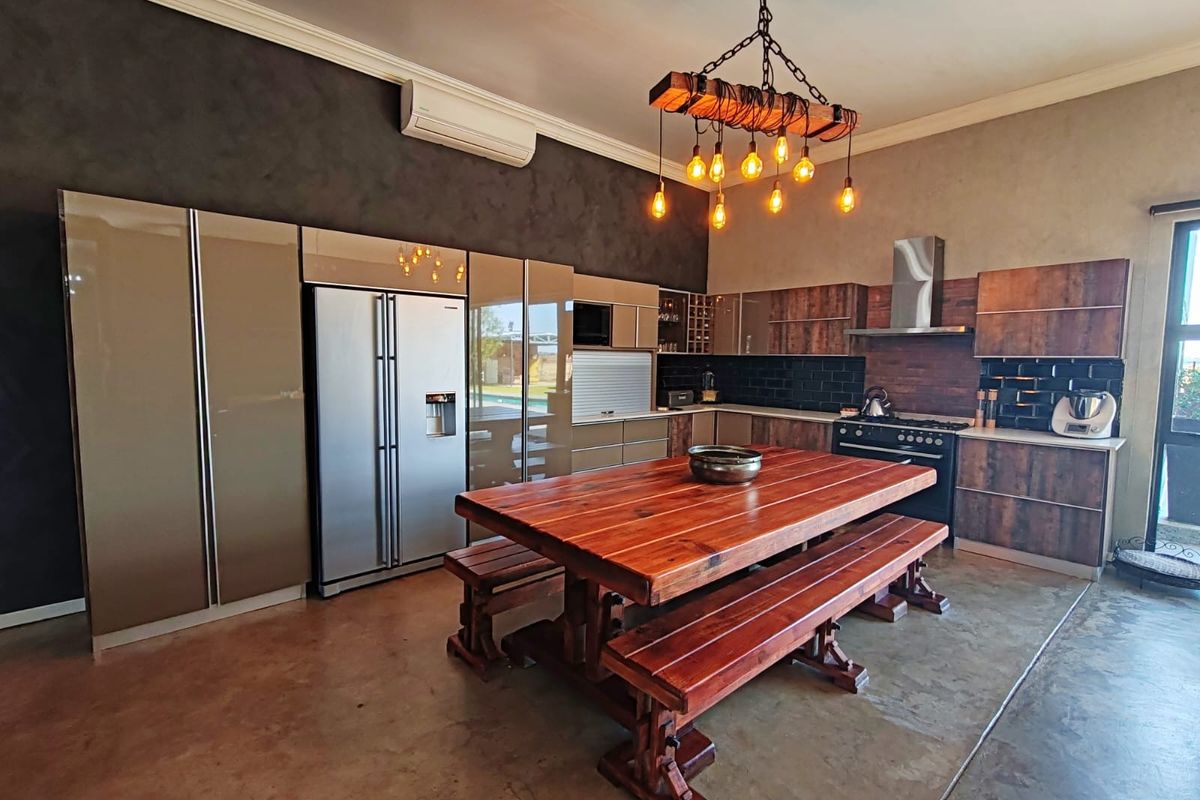 Modern kitchen featuring high-gloss cabinetry, wood-finish cupboards, a stainless steel extractor fan, and a central wooden dining area with polished concrete flooring.