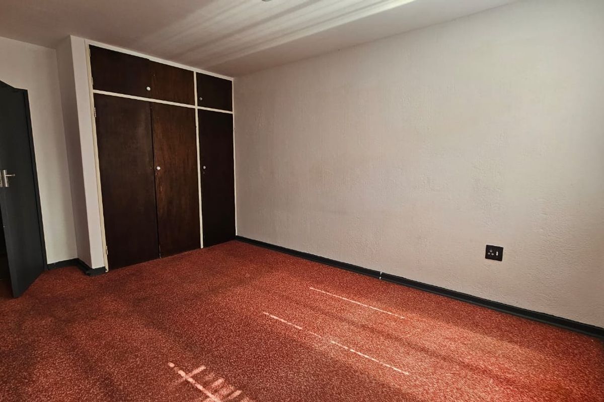 A vacant bedroom featuring dated built-in wooden cupboards and worn carpeting, offering a blank canvas for potential renovation and modernization.