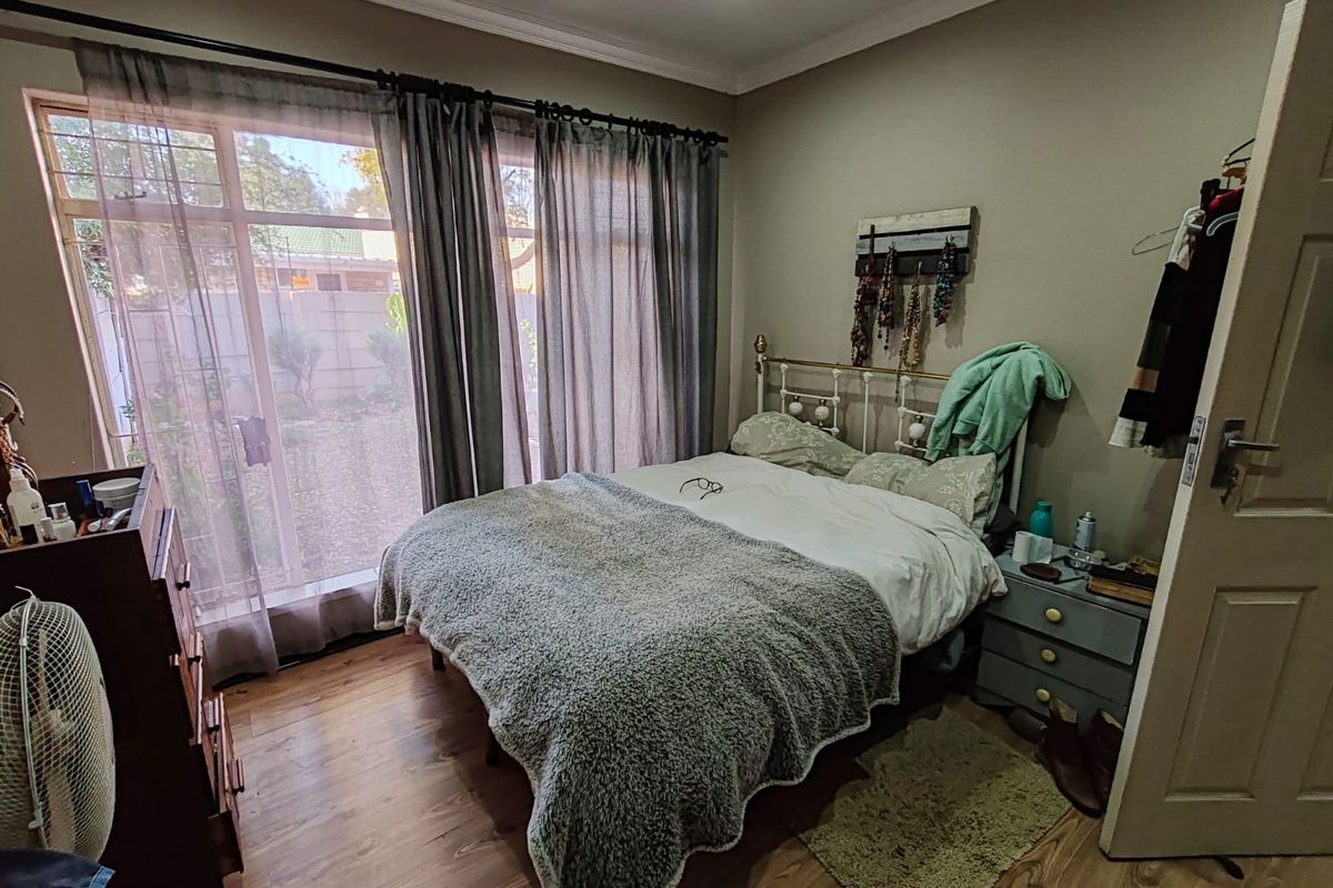 A cozy bedroom featuring laminate flooring, large sliding glass doors providing natural light, and access to the exterior garden area.