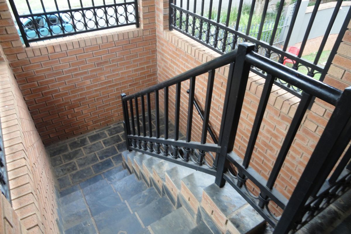 An outdoor staircase featuring face brick walls, dark stone tiling, and black metal security railings.
