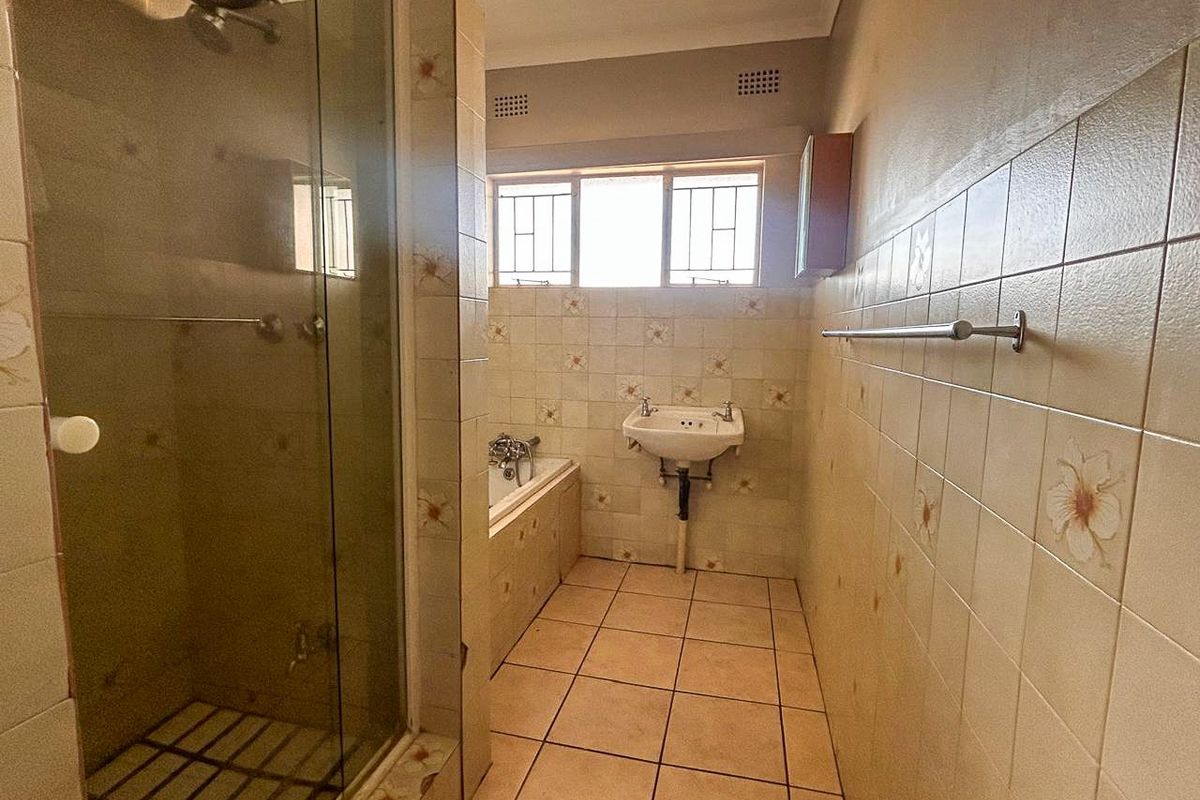 A dated bathroom featuring a separate shower enclosure, a built-in bathtub, and a wall-mounted basin with original ceramic tiling throughout.