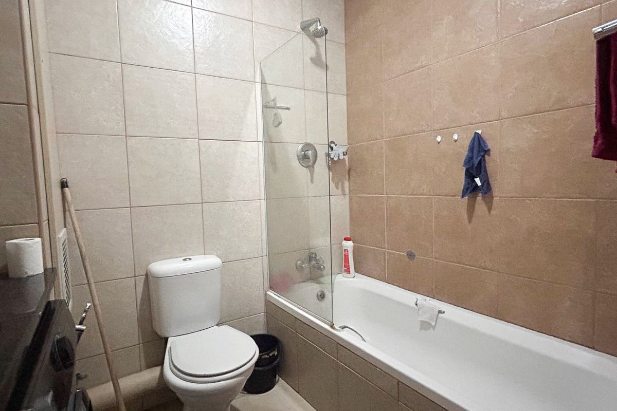 A functional bathroom featuring a bathtub with a glass shower screen, wall-mounted shower head, and a standard toilet.