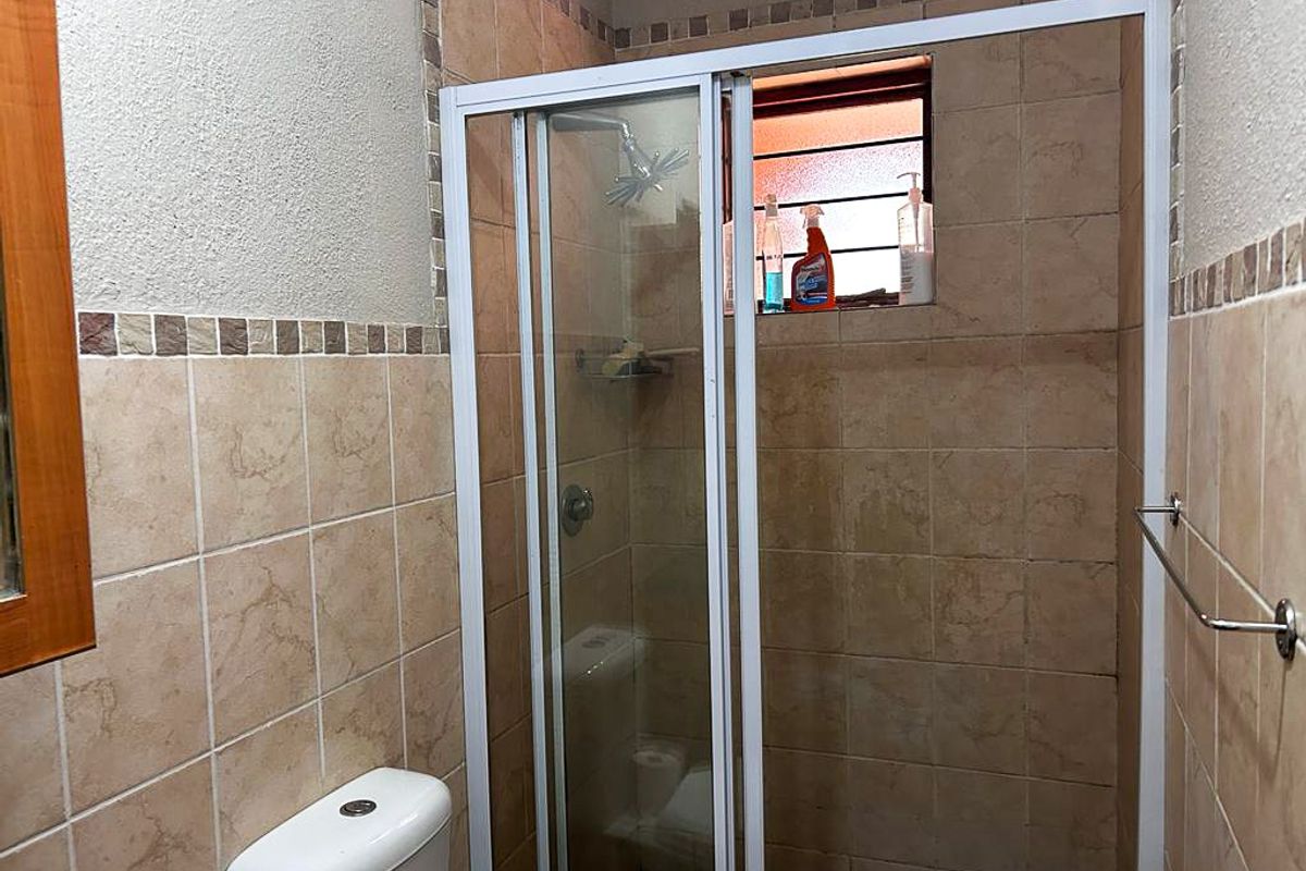 A functional bathroom featuring a tiled shower enclosure with a sliding glass door, a toilet, and a wall-mounted towel rail.