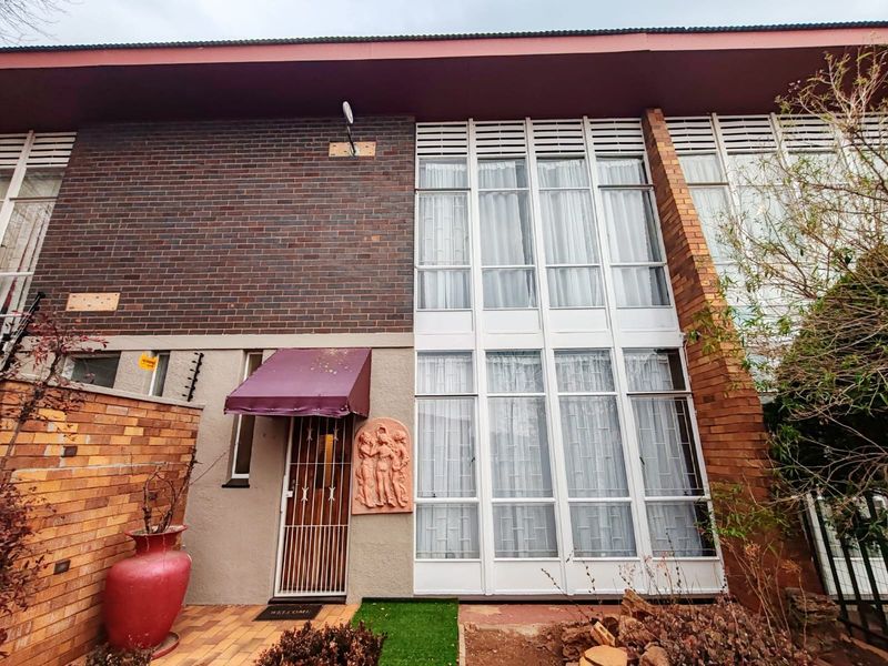 Front facade of a townhouse featuring a brick exterior, large floor-to-ceiling windows, and a secure metal entrance gate with a decorative wall relief.