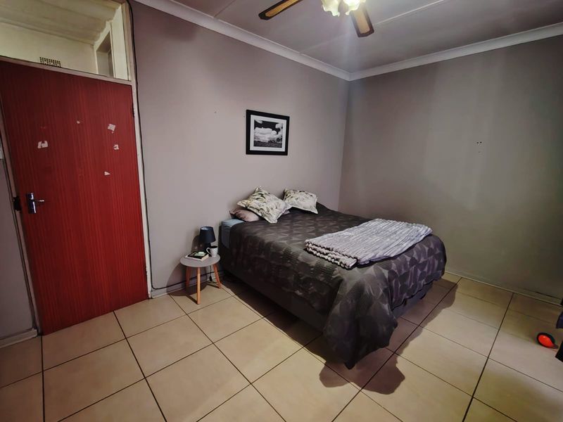 A bedroom featuring tiled flooring, a ceiling fan, and a solid wood door with a transom window above.