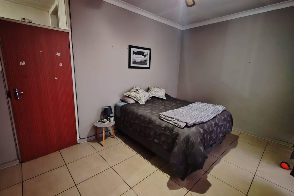 A bedroom featuring tiled flooring, a ceiling fan, and a solid wood door with a transom window above.