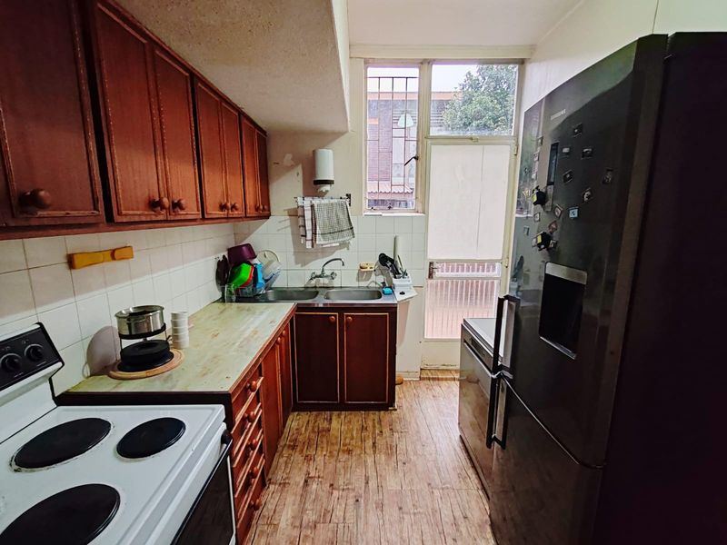 A compact kitchen featuring wooden cabinetry, tiled splashbacks, a double sink, and direct access to an exterior door.