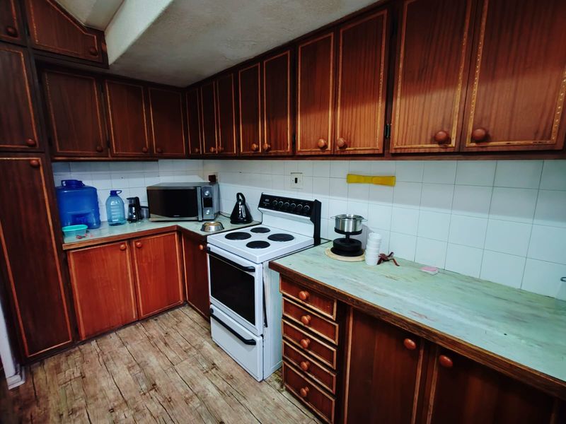 A dated kitchen featuring traditional wood-finish cabinetry, white tiled splashbacks, and a freestanding electric stove, offering a functional layout with ample storage space.