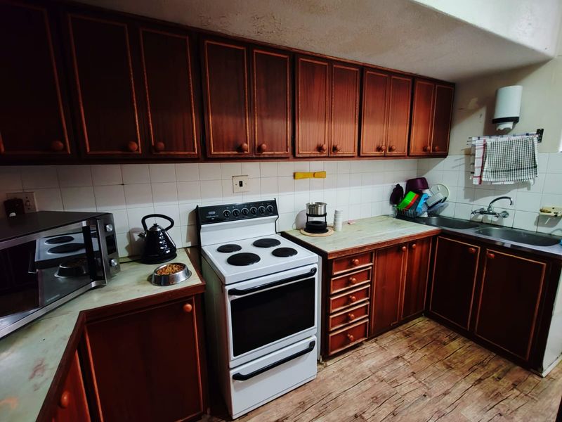 A dated kitchen featuring dark wood cabinetry, a freestanding stove, and laminate countertops with a tiled backsplash.