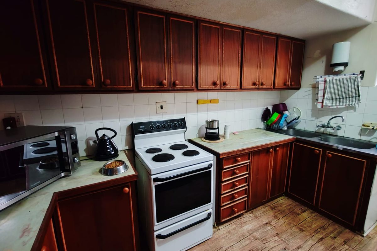 A dated kitchen featuring dark wood cabinetry, a freestanding stove, and laminate countertops with a tiled backsplash.