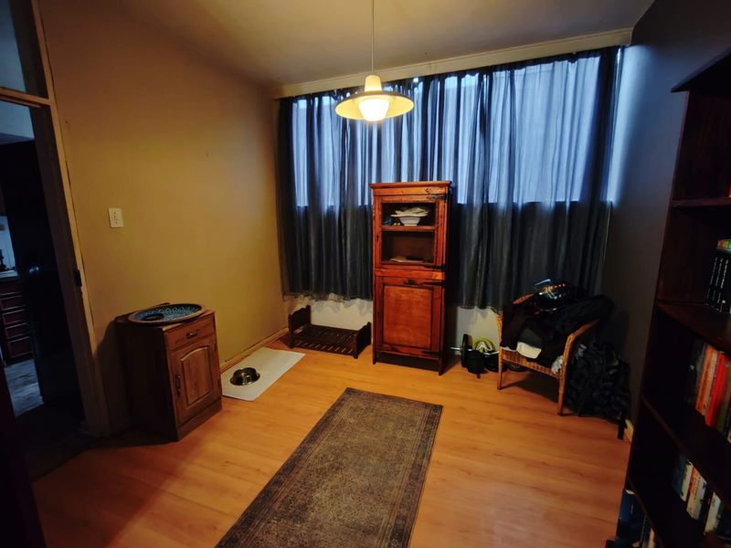 A functional living room space featuring laminate flooring, a large window with curtains, and a central pendant light fixture.