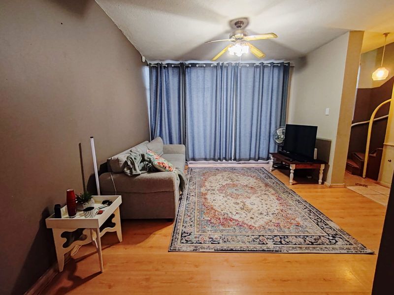 A living room featuring laminate flooring, a ceiling fan, and large sliding doors covered by curtains, leading to an adjacent staircase area.
