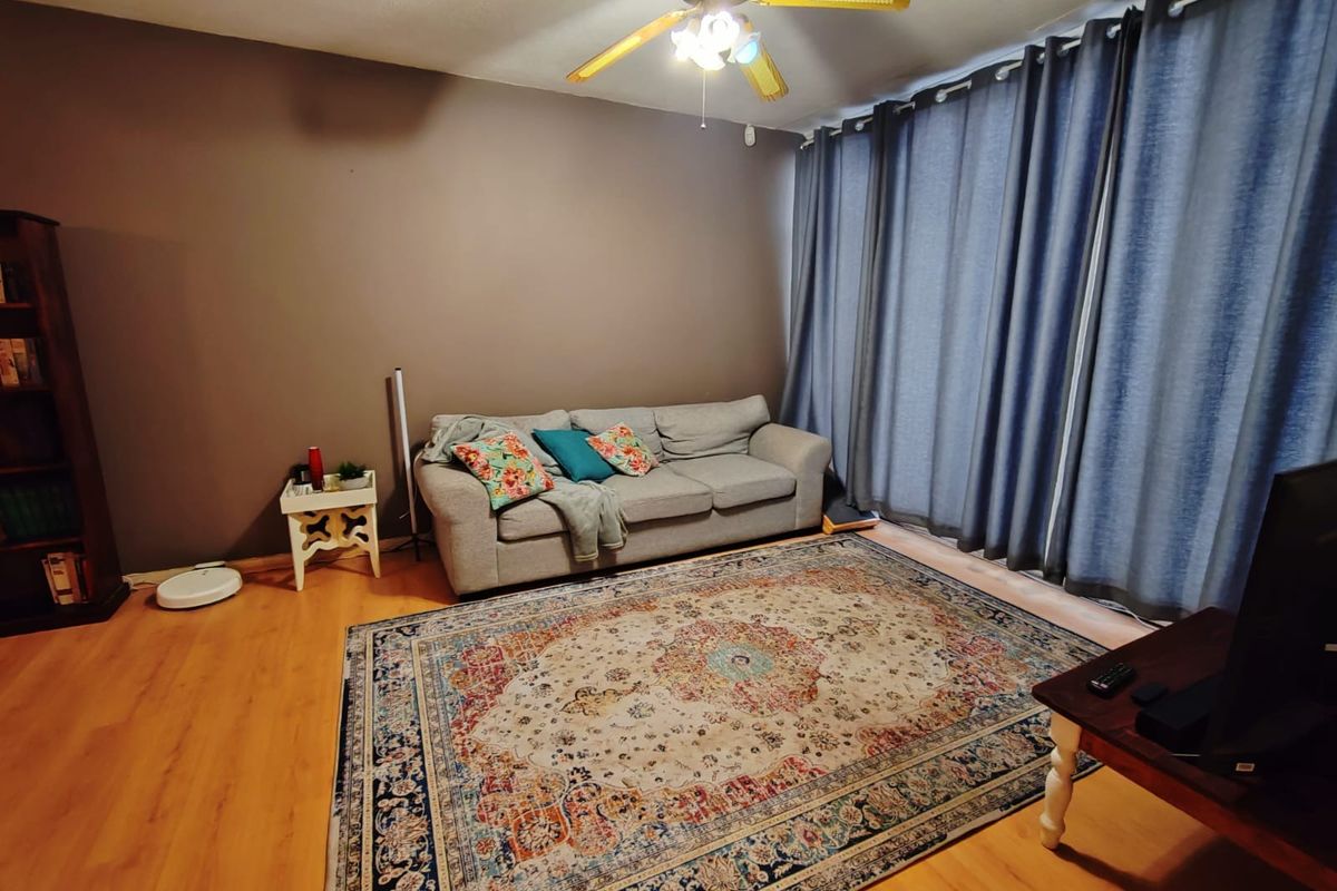A living room featuring laminate wood flooring, a ceiling fan, and floor-to-ceiling curtains covering a large window or sliding door.
