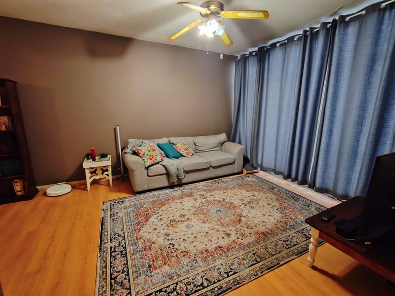 A living room featuring laminate wood flooring, a ceiling fan, and floor-to-ceiling curtains covering a large window or sliding door.