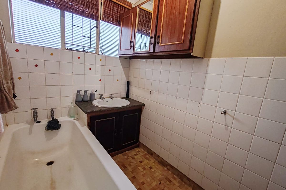 A dated bathroom featuring a built-in bathtub, vanity cabinet with integrated basin, and tiled wall finishes.