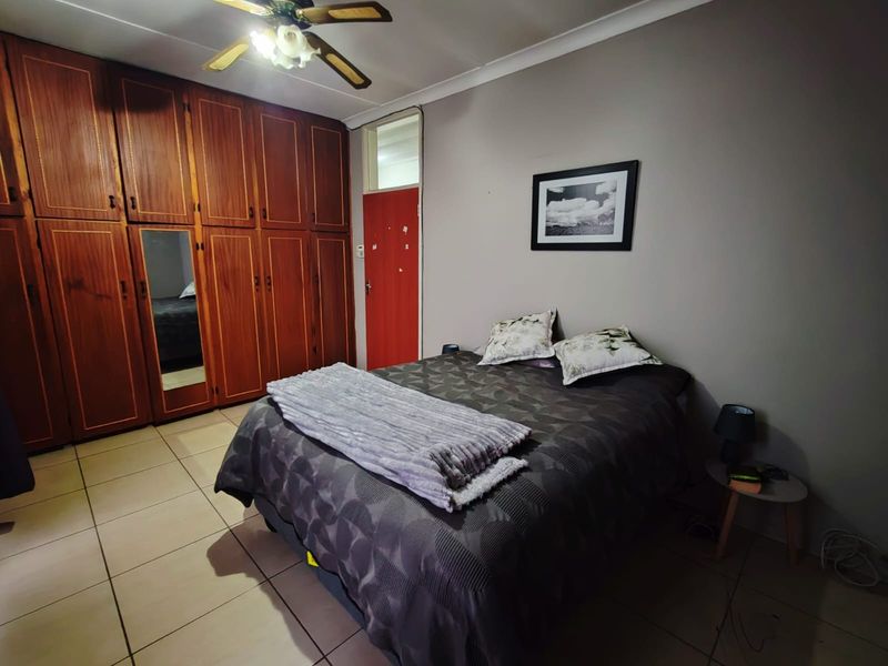 A bedroom featuring built-in wooden wardrobes, tiled flooring, and a ceiling fan, offering functional storage space.