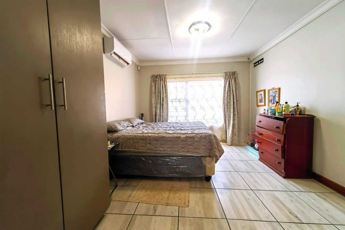 A bedroom featuring tiled flooring, built-in cupboards, and a wall-mounted air conditioning unit.