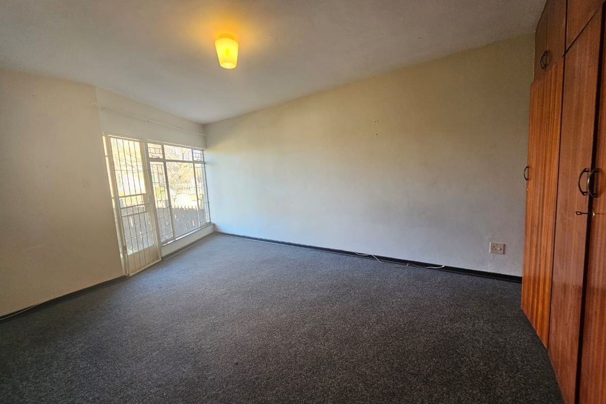 A spacious, empty bedroom featuring built-in wooden cupboards, grey carpeting, and a security gate leading to an outdoor area.
