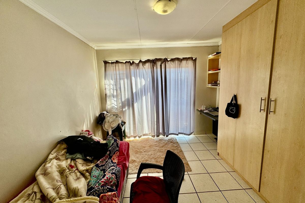 A bedroom featuring built-in wooden cupboards, tiled flooring, and a sliding door leading to an outdoor area.