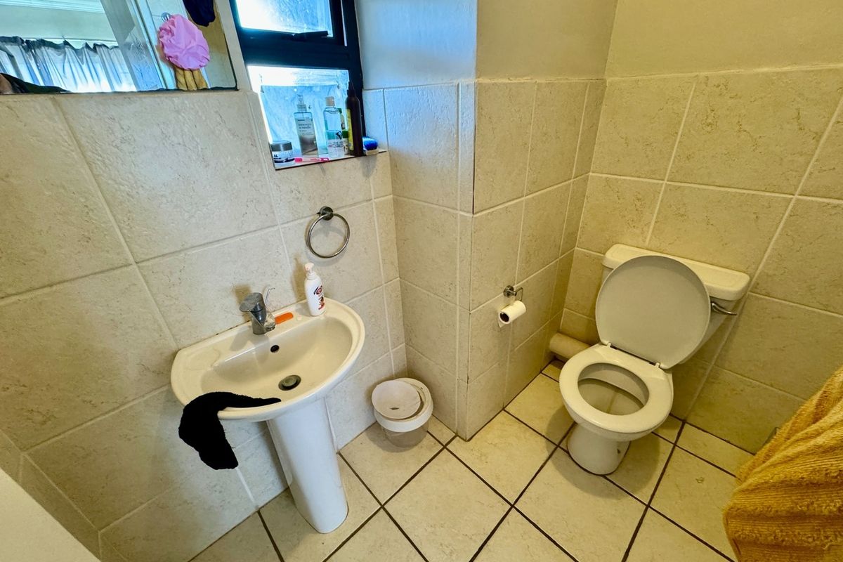 A functional bathroom featuring a pedestal basin, a standard toilet, and neutral wall and floor tiling.