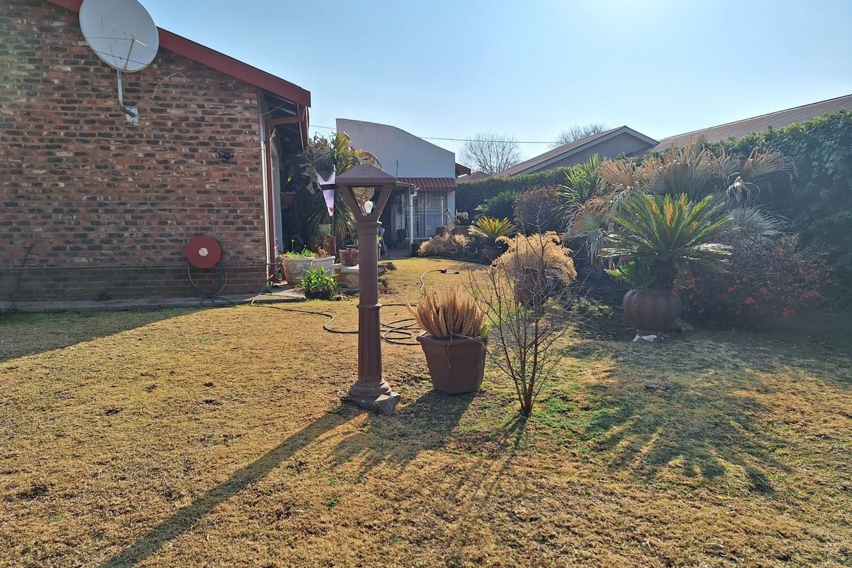 A view of the rear garden area featuring a brick exterior wall, established landscaping, and a fixed garden lamp post.
