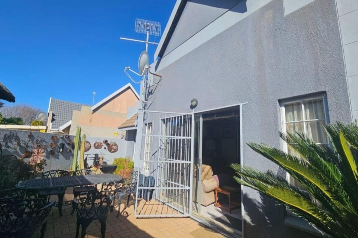 A rear patio area featuring paved flooring, a security gate, and exterior wall access to the main living space.
