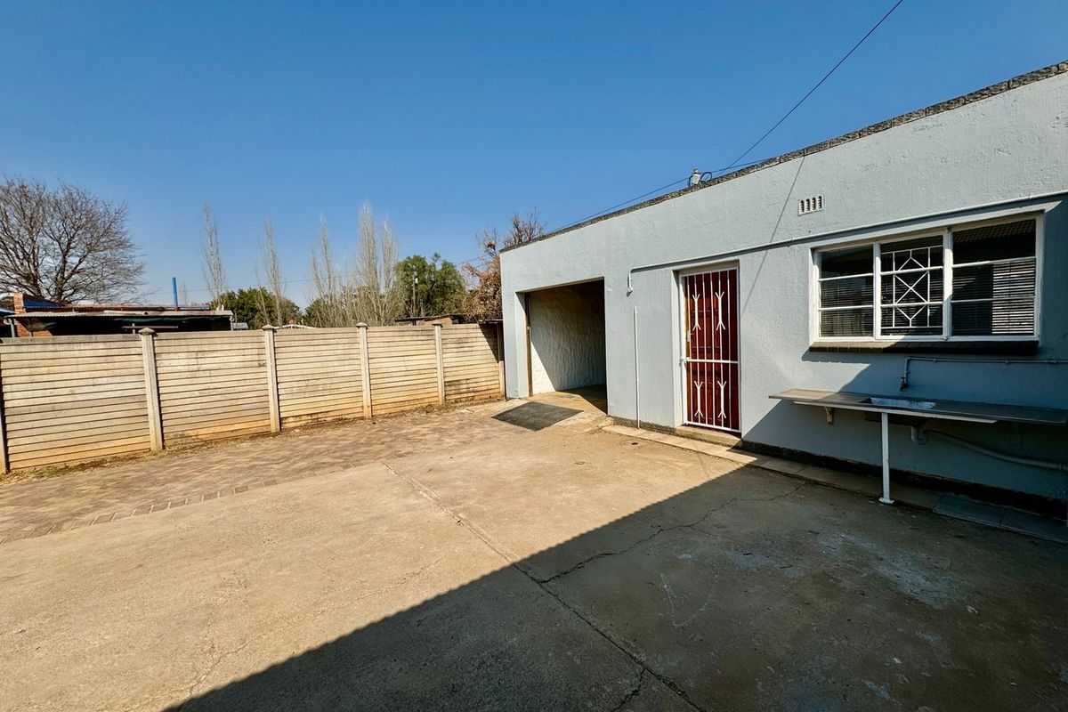 Rear exterior view featuring a concrete courtyard, a single garage entrance, a security gate, and a wall-mounted utility sink.