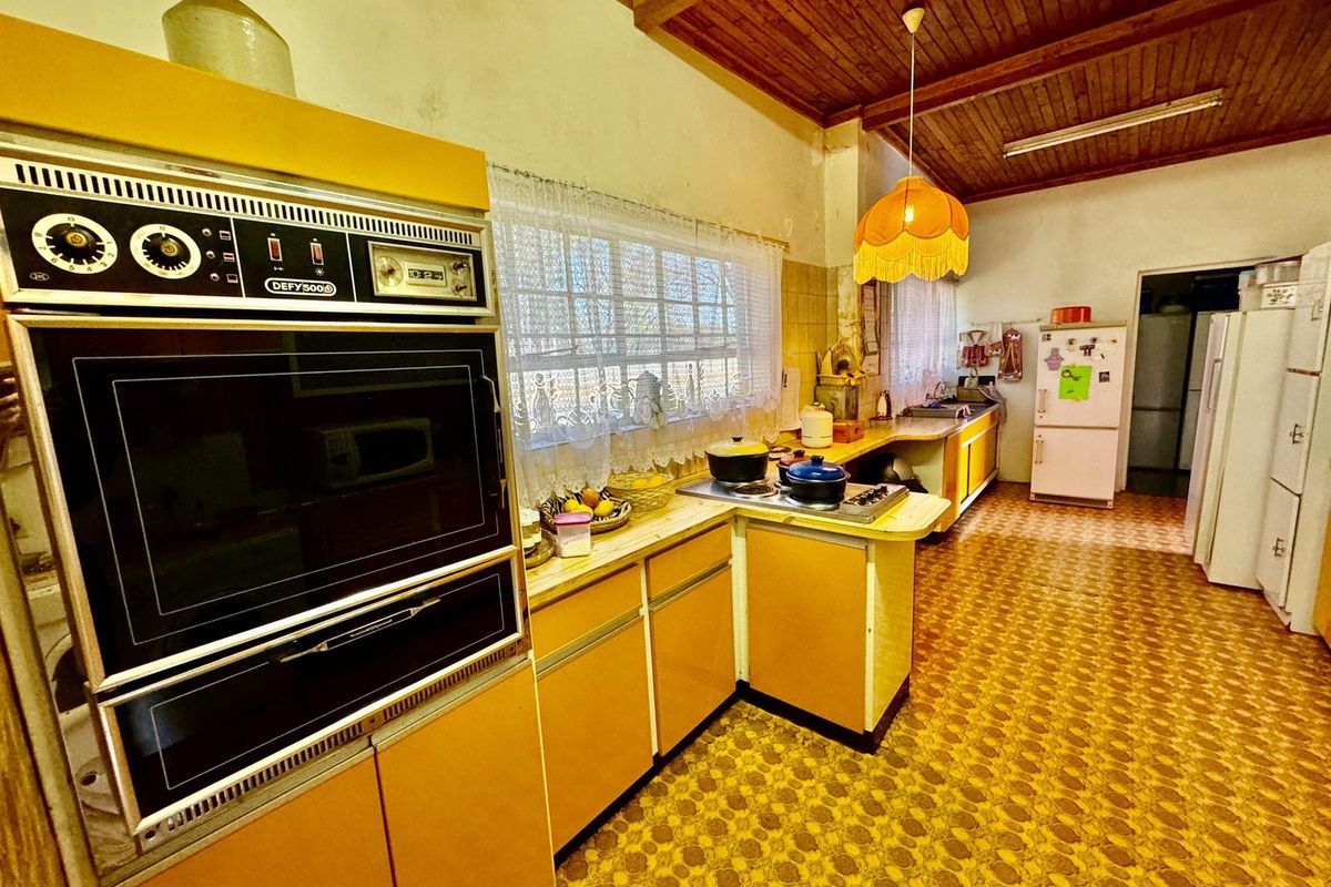 A vintage-style kitchen featuring original cabinetry, a built-in Defy oven, and exposed timber ceiling beams, offering significant potential for a modern renovation.