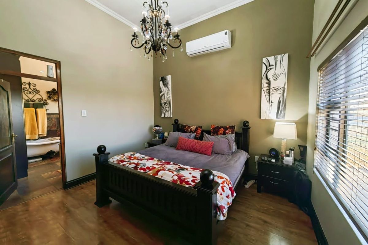A well-maintained bedroom featuring laminate flooring, a split-system air conditioner, and a decorative chandelier, with an adjoining en-suite bathroom visible.