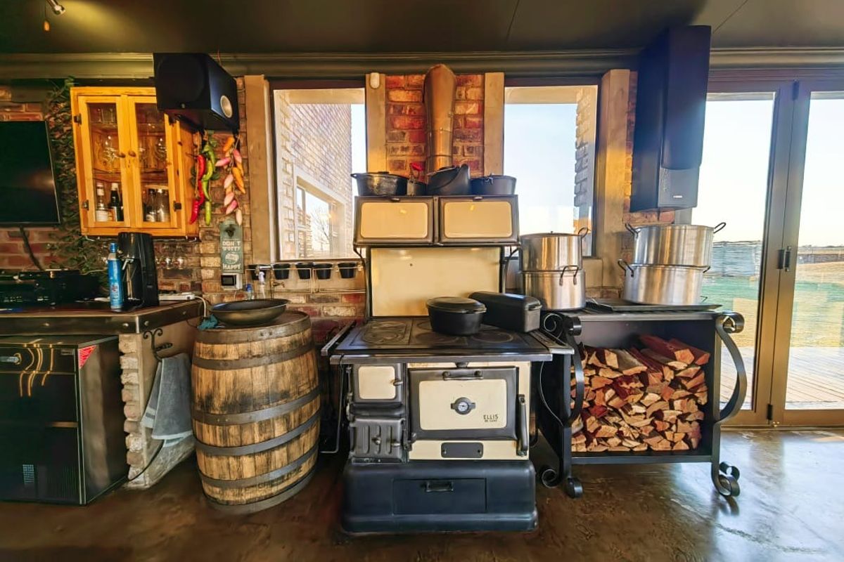 A rustic kitchen area featuring an antique-style cast iron stove, exposed brick walls, and polished concrete flooring with access to an outdoor deck.