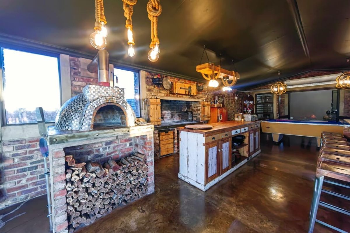 Spacious entertainment area featuring a built-in pizza oven, exposed brick walls, polished concrete floors, and custom cabinetry in a rustic industrial style.