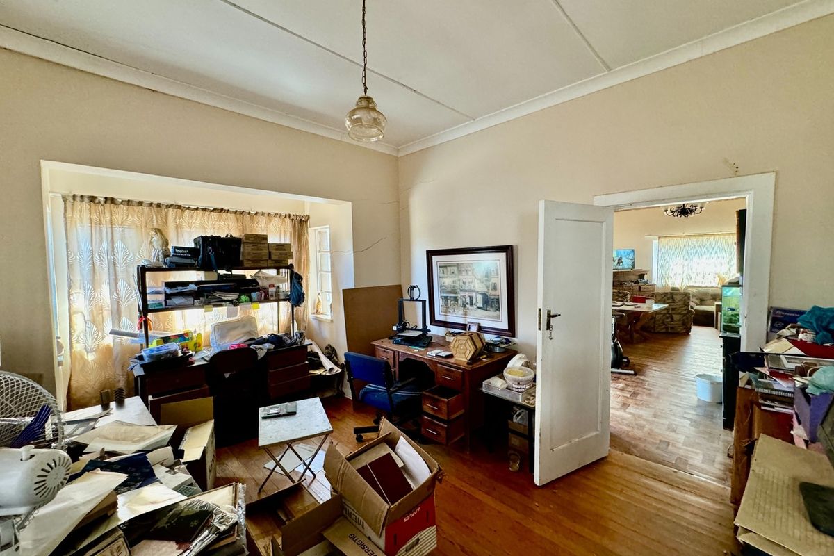 A living room featuring original timber parquet flooring, a large window with natural light, and a doorway leading to an adjacent living space.