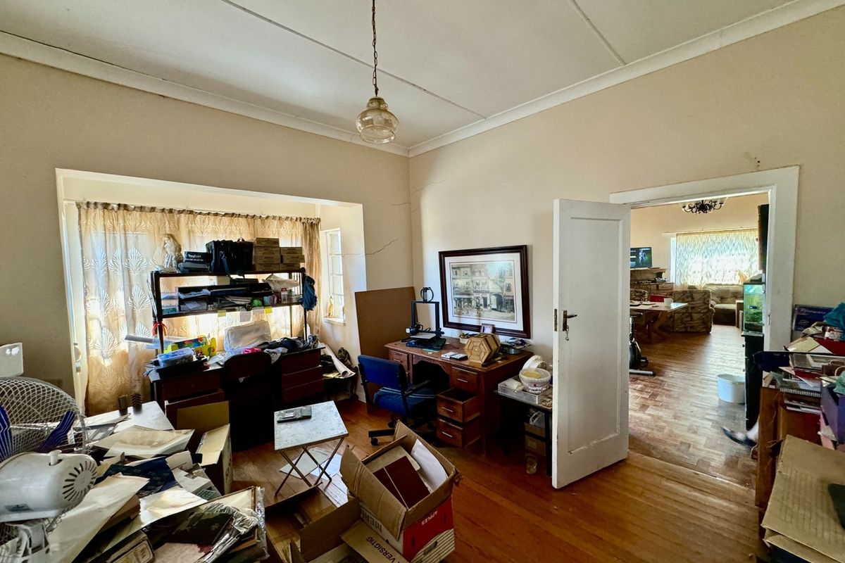 A multi-purpose room featuring original timber flooring, a classic pendant light fixture, and a large window, offering potential for a home office or bedroom.