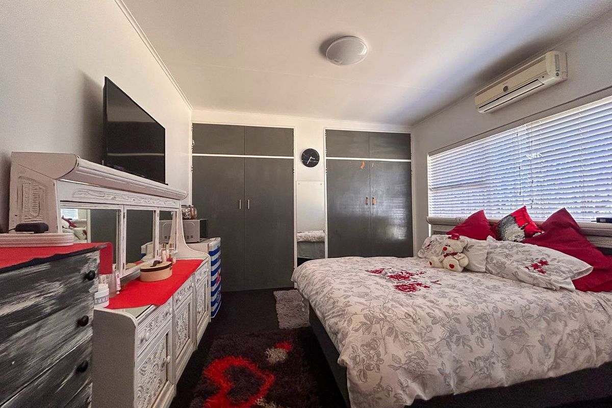 A bedroom featuring built-in cupboards, a wall-mounted air conditioning unit, and large windows with fitted blinds.