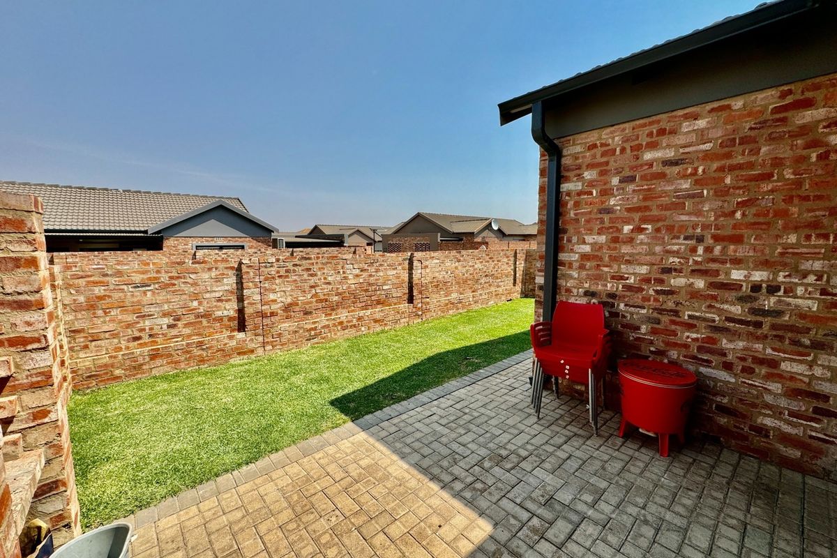 A private rear garden featuring a paved patio area and a well-maintained lawn, enclosed by face-brick boundary walls.
