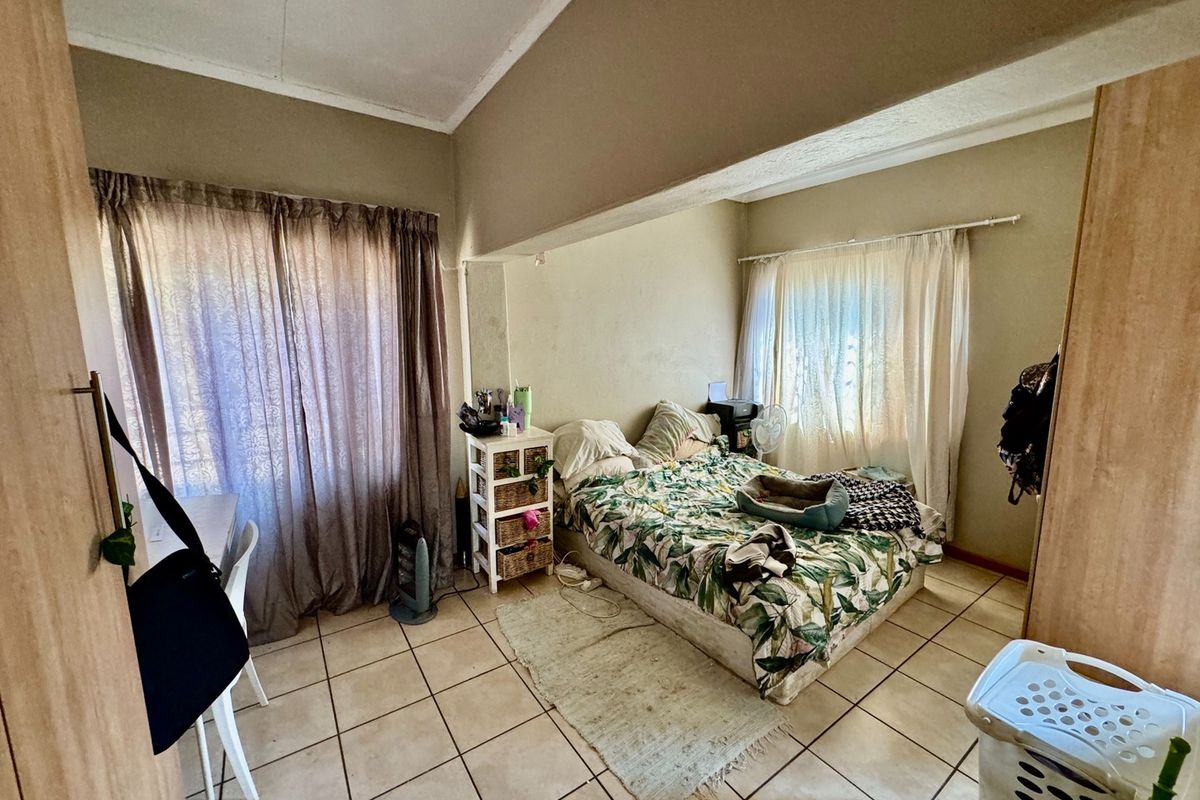 A bedroom featuring tiled flooring, built-in cupboards, and dual window access with curtain fixtures.