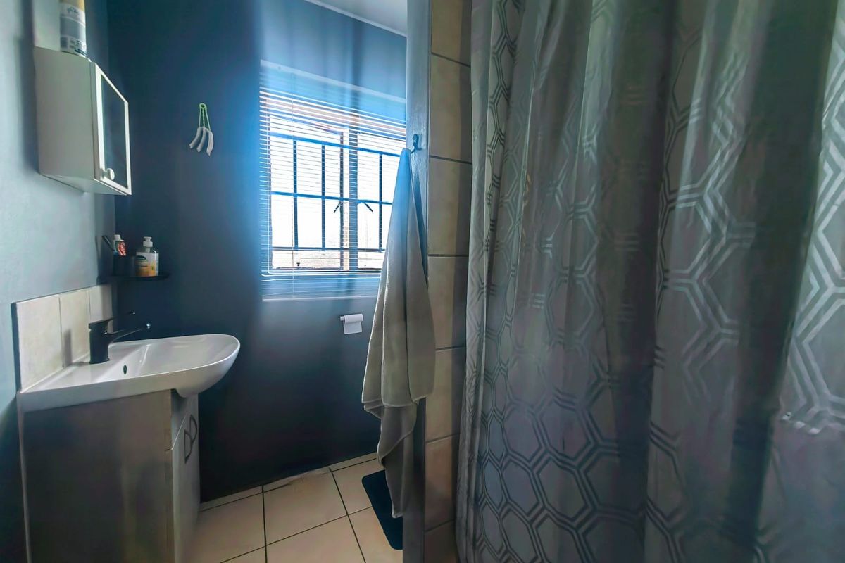 A functional bathroom featuring a vanity basin, tiled flooring, and a shower area with a curtain, illuminated by natural light from a window.