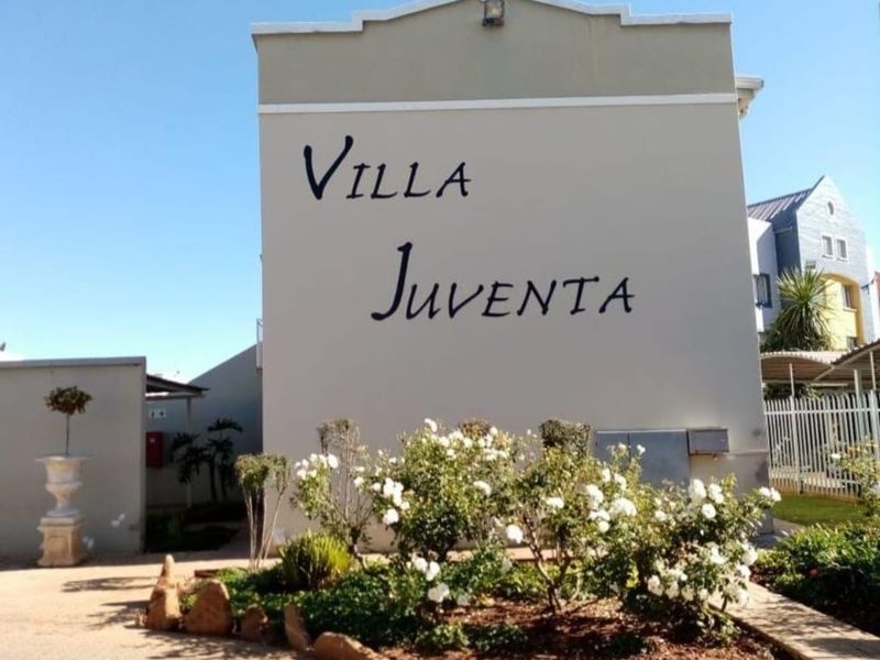 Exterior view of the Villa Juventa apartment complex entrance, featuring a landscaped garden bed and clear building signage.