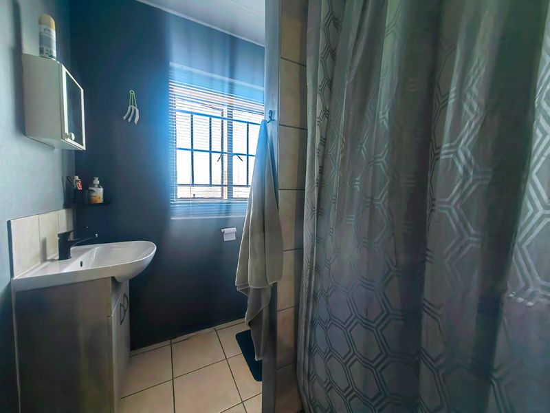 A functional bathroom featuring a vanity basin, tiled flooring, and a shower area with a curtain, illuminated by natural light from a window.